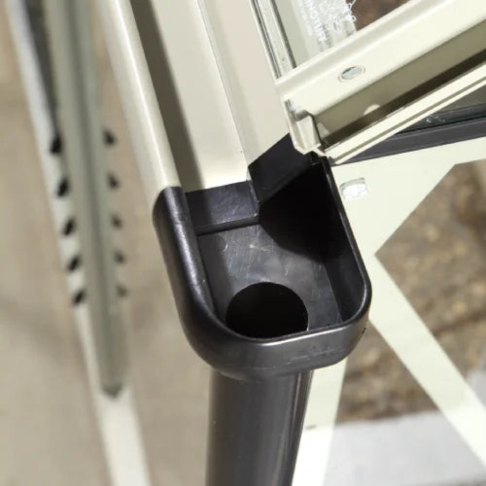 A metal frame connector holds structural elements together, showcasing a sleek, black and beige finish. It is part of a Rhino Greenhouse assembly, installed on a concrete surface.