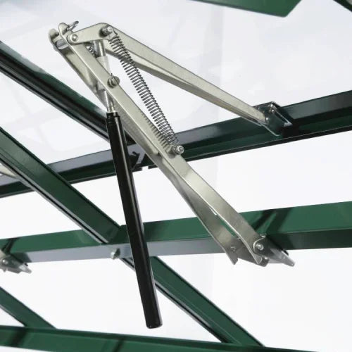 A metal window opener, equipped with a spring mechanism, lifts a section of Rhino Greenhouse glass. The structure features green metal framing and is set in a well-lit environment.