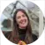 A person smiling while standing in front of Rhino Greenhouse structures, with blurred greenery in the background.